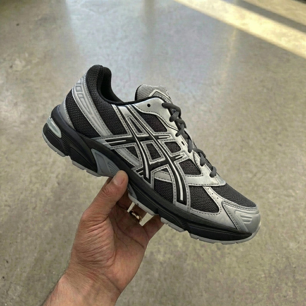 ASICS Gel-1130 Graphite Grey Gravel held in man's hand showing graphite grey mesh upper with synthetic overlays and EVA midsole with GEL insert against polished concrete background