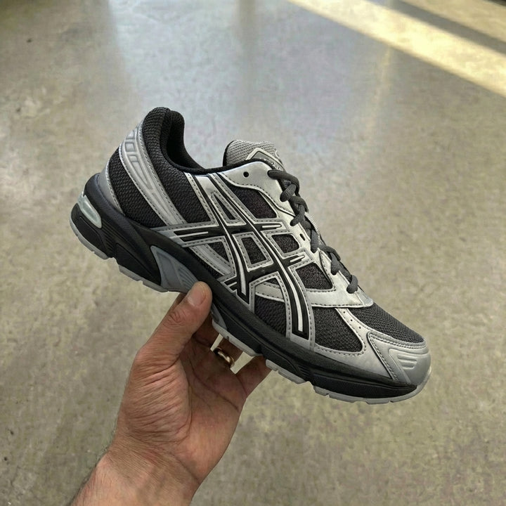 ASICS Gel-1130 Graphite Grey Gravel held in man's hand showing graphite grey mesh upper with synthetic overlays and EVA midsole with GEL insert against polished concrete background