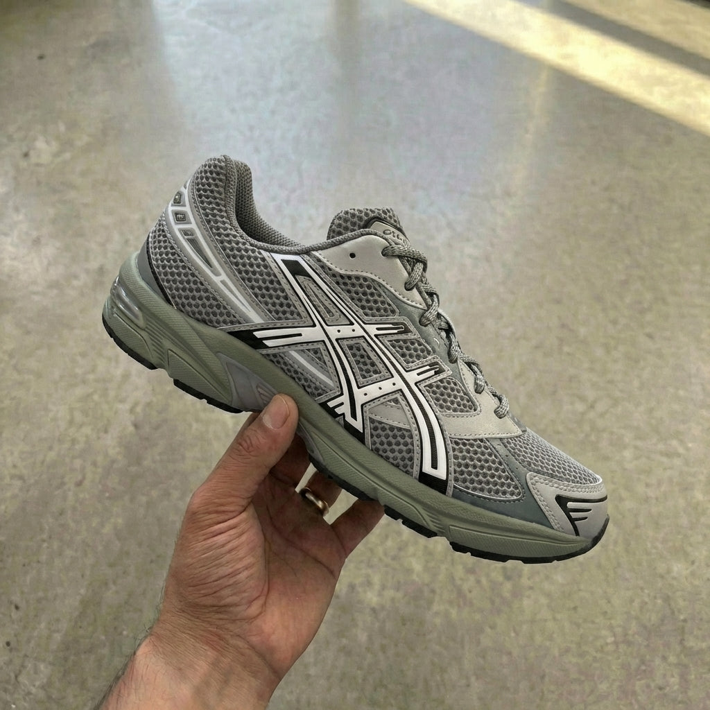 ASICS Gel-1130 Wild Dove held in man's hand showing dove grey mesh upper with synthetic overlays and EVA midsole with GEL insert against polished concrete background