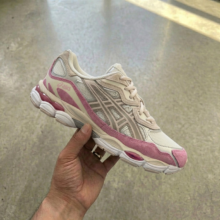 ASICS Gel-NYC Cream Mineral Beige Pink held in man's hand showing cream mesh upper with suede and leather overlays, pink suede toe wrap, and metallic silver side panels against polished concrete background