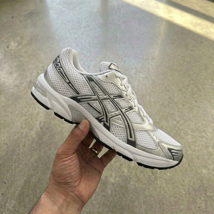 ASICS Gel-1130 White Pure Silver held in man's hand showing white mesh upper with pure silver ASICS logo and synthetic overlays against polished concrete background
