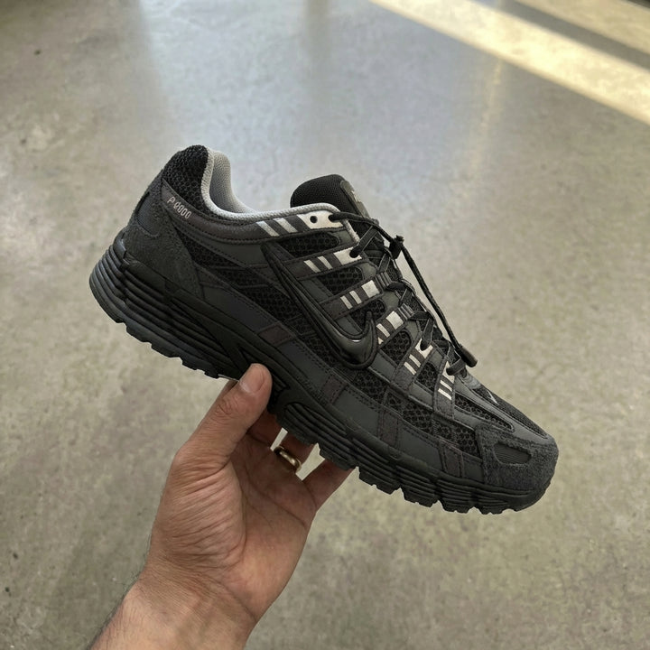 Nike P-6000 Anthracite Metallic Silver held in man's hand showing anthracite textile upper with metallic silver accents against polished concrete background