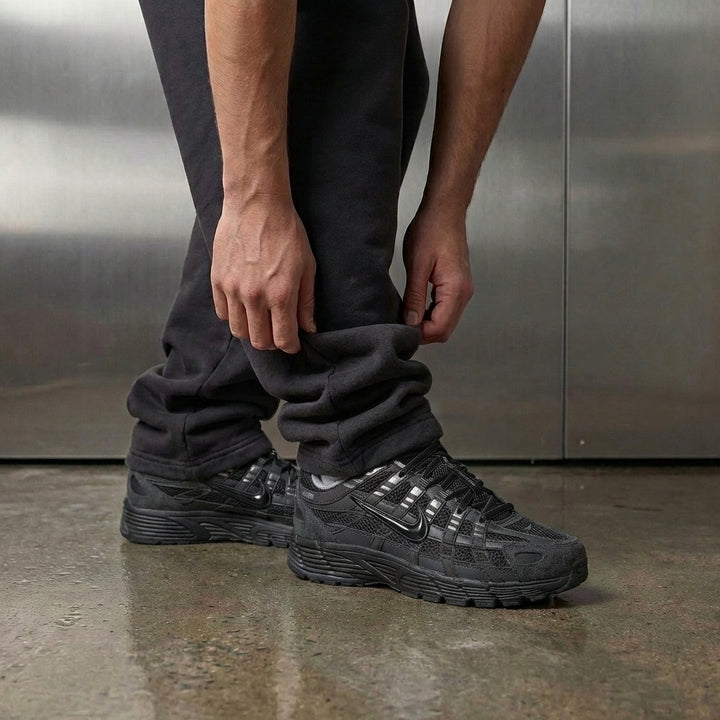 Nike P-6000 Anthracite Metallic Silver on foot, man adjusting jogger cuff to reveal anthracite upper with metallic silver accents and foam midsole, industrial studio with stainless steel backdrop and polished concrete floor