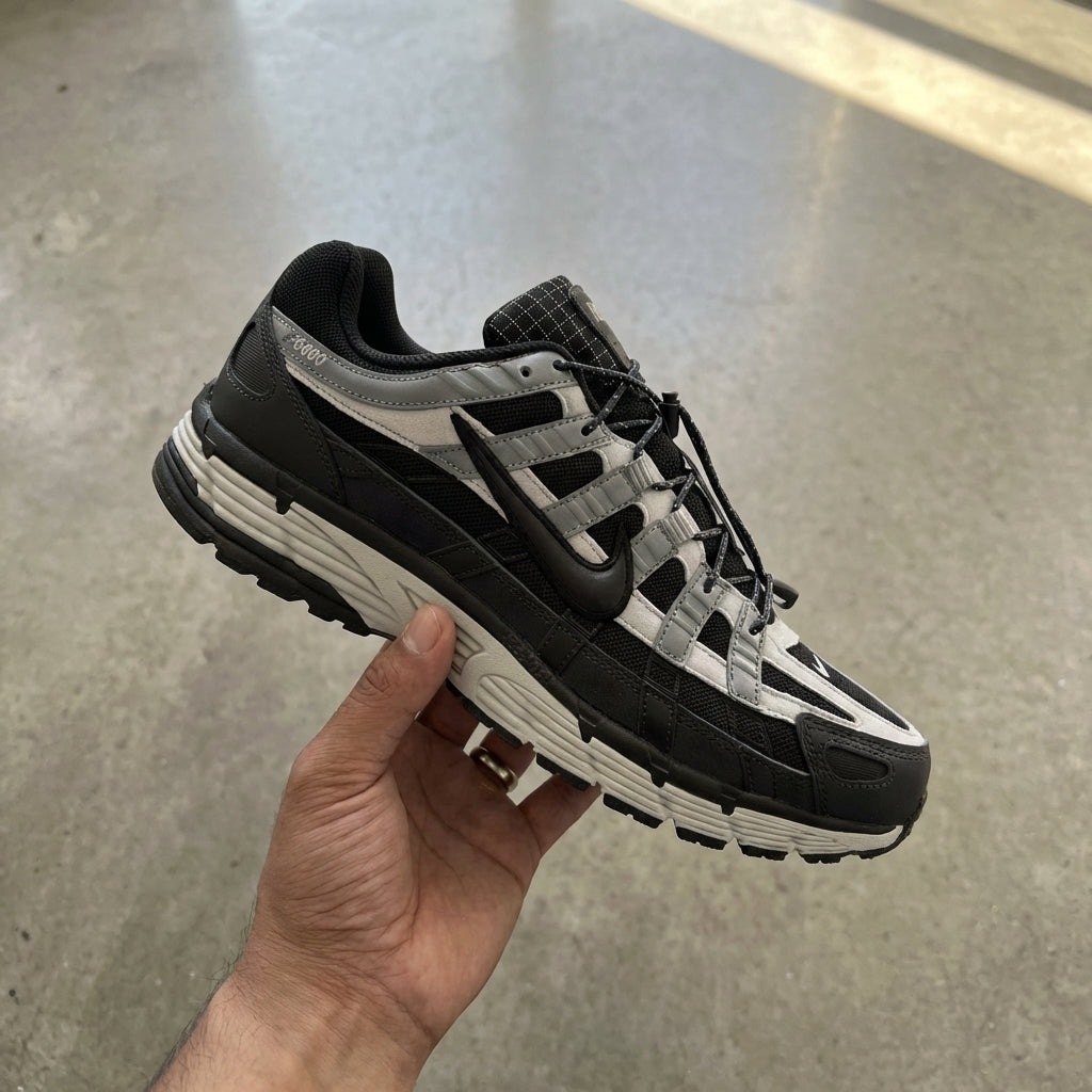 Nike P-6000 Anthracite Smoke Grey held in man's hand showing anthracite textile upper with leather overlays and smoke grey accents against polished concrete background