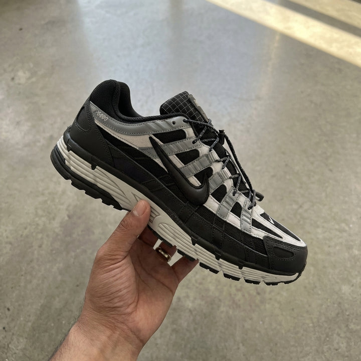 Nike P-6000 Anthracite Smoke Grey held in man's hand showing anthracite textile upper with leather overlays and smoke grey accents against polished concrete background