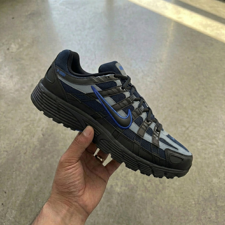 Nike P-6000 Black Obsidian held in man's hand showing black mesh upper with obsidian synthetic overlays and cool grey accents against polished concrete background