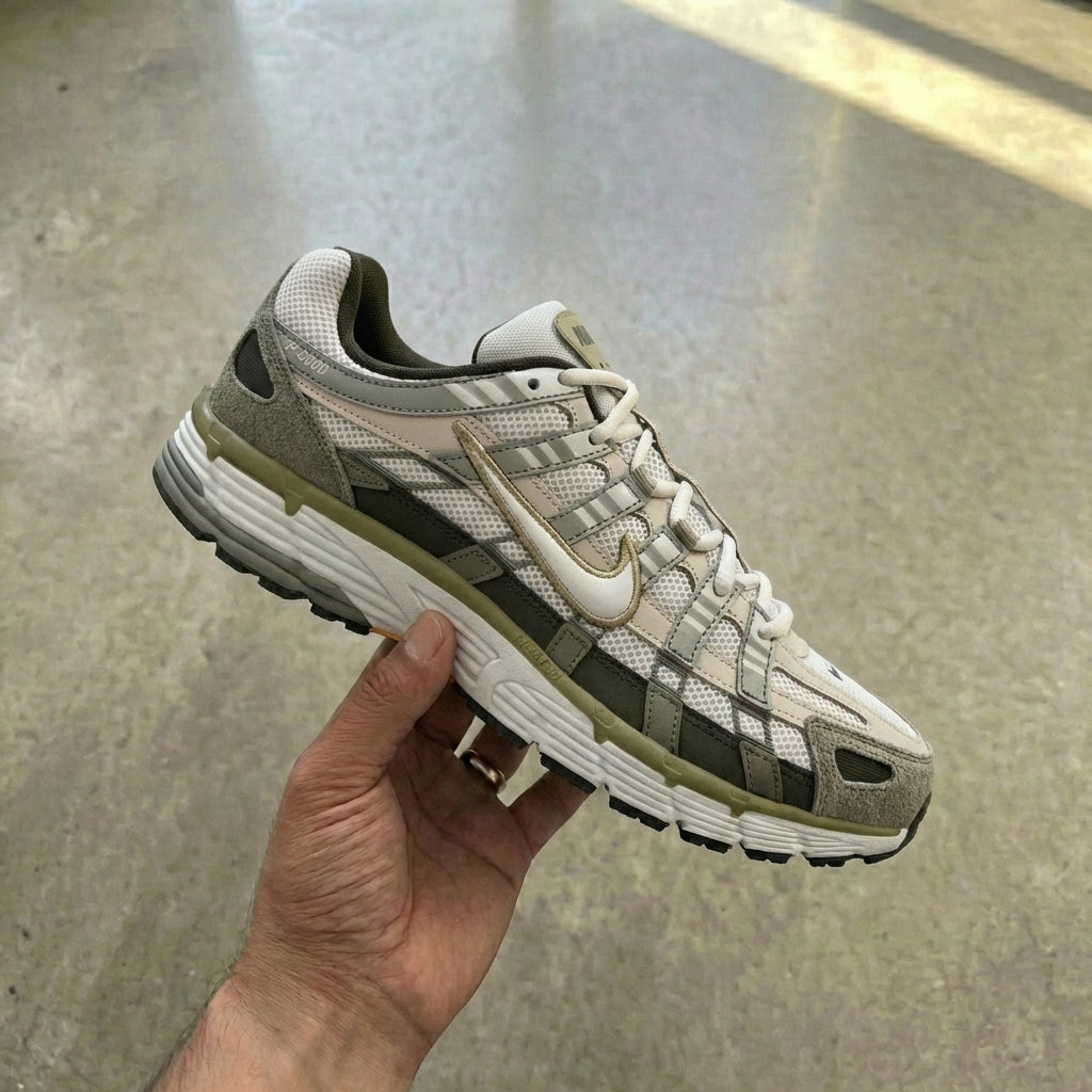Nike P-6000 Cargo Khaki held in man's hand showing cargo khaki mesh upper with leather and synthetic overlays in earth tones against polished concrete background