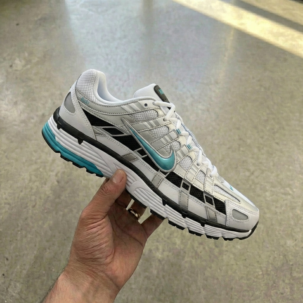 Nike P-6000 Dusty Cactus held in man's hand showing white mesh upper with metallic silver and Dusty Cactus aqua leather overlays against polished concrete background