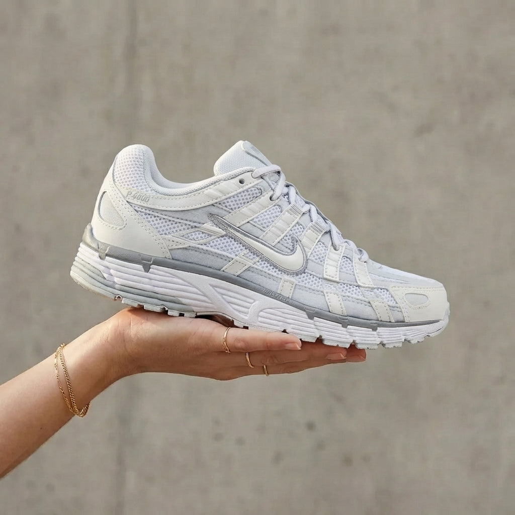 Nike P-6000 Summit White Pure Platinum held in woman's hand showing summit white mesh upper with pure platinum synthetic overlays against polished concrete background

