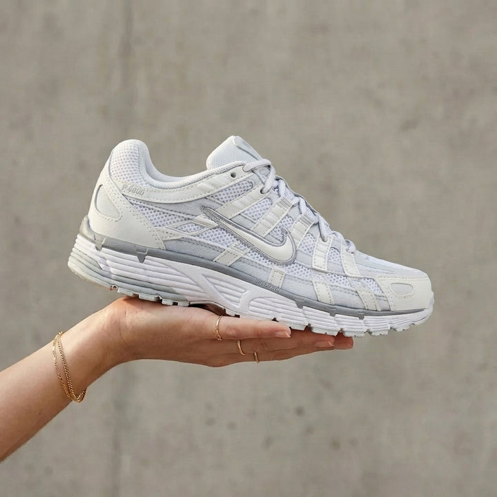 Nike P-6000 Summit White Pure Platinum held in woman's hand showing summit white mesh upper with pure platinum synthetic overlays against polished concrete background
