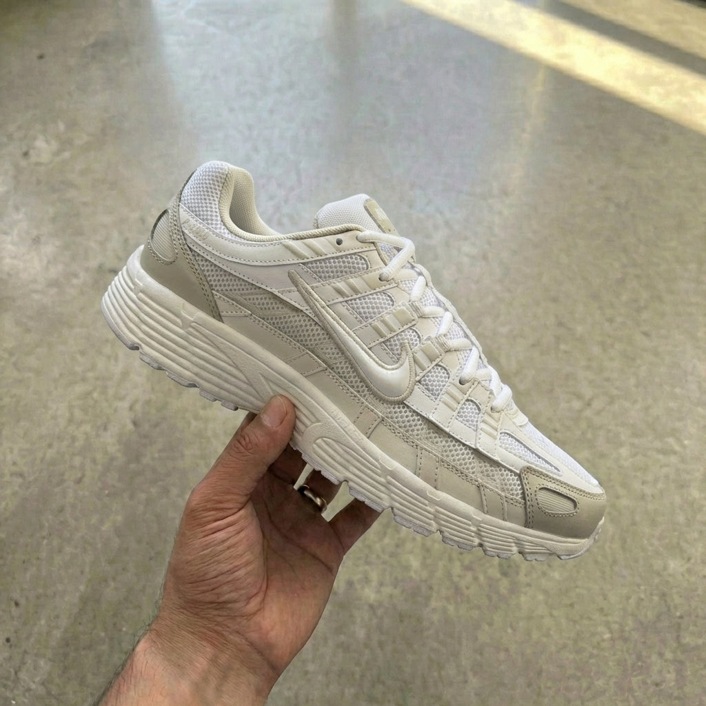 Nike P-6000 White Sail held in man's hand showing white mesh upper with sail cream synthetic overlays and vast grey accents against polished concrete background