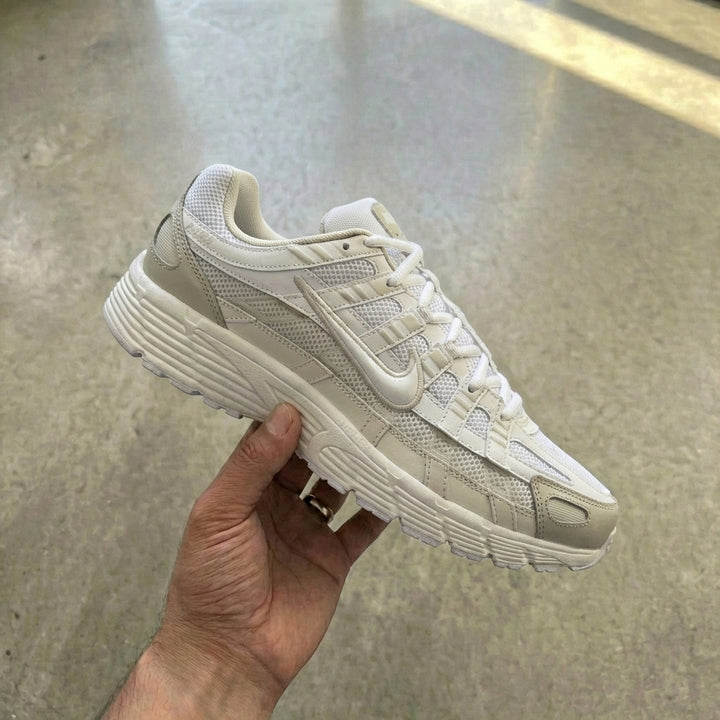 Nike P-6000 White Sail held in man's hand showing white mesh upper with sail cream synthetic overlays and vast grey accents against polished concrete background